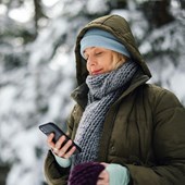 En kvinna läser på en mobil i ett vinterlandskap