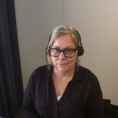 Kinna i gråsvart kofta med headset framför en skärm