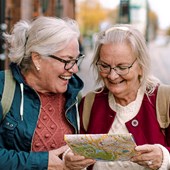 Två äldre damer som tittar på en karta och ler. 