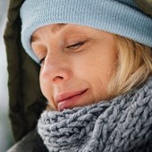 Kvinna med vinterkläder. Snötäckta träd i bakgrunden.
